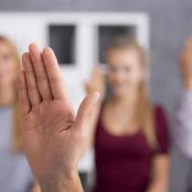 Close up of a hand in a welcome gesture, in the background blurred image of three people